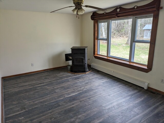 empty room featuring a wood stove, a baseboard radiator, ceiling fan, baseboards, and dark wood finished floors