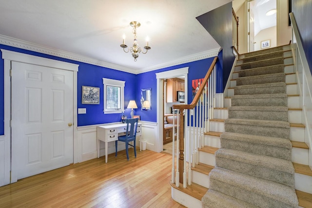 stairway with wainscoting, wood finished floors, a chandelier, and crown molding