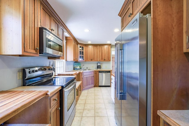 kitchen featuring brown cabinets, glass insert cabinets, light tile patterned floors, stainless steel appliances, and recessed lighting