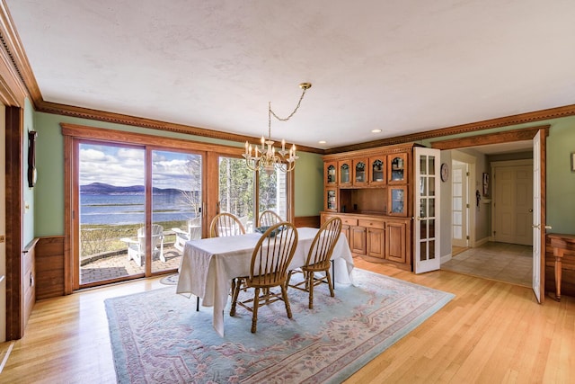 dining area with light wood finished floors, a water view, crown molding, and an inviting chandelier