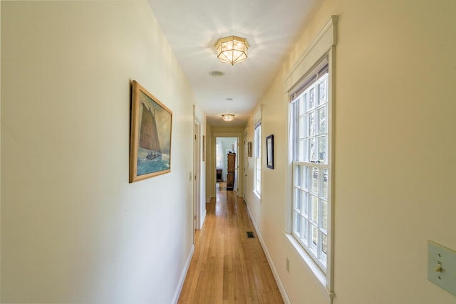 corridor featuring light wood finished floors, baseboards, and visible vents