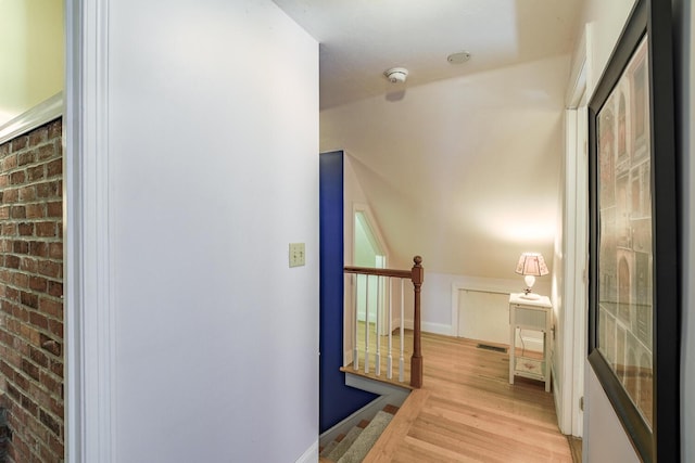 hall featuring light wood-style flooring, visible vents, baseboards, and an upstairs landing