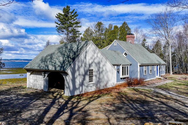 view of property exterior with a shingled roof, a chimney, and a water view