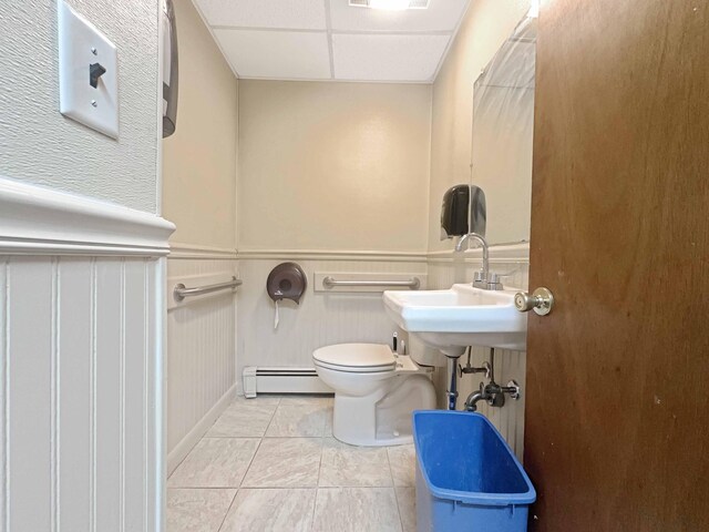 1716 Main St, Mapleton, ME 04757 - half bathroom featuring baseboard heating, tile patterned flooring, toilet, wainscoting, and a decorative wall