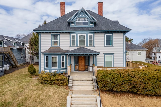 american foursquare style home with a chimney, a shingled roof, and a front lawn