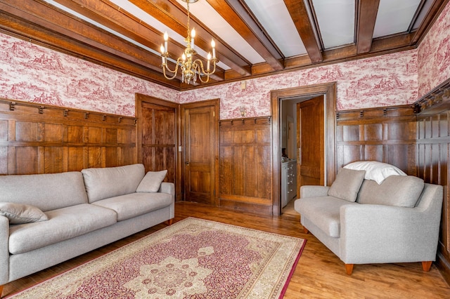 living area featuring beam ceiling, an inviting chandelier, wainscoting, and wallpapered walls