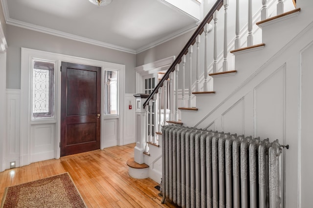 entryway featuring hardwood / wood-style floors, a decorative wall, radiator heating unit, and stairway