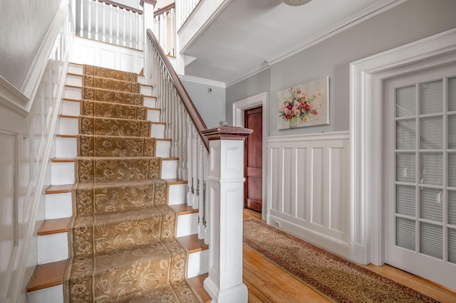 staircase featuring a decorative wall, ornamental molding, and wood finished floors