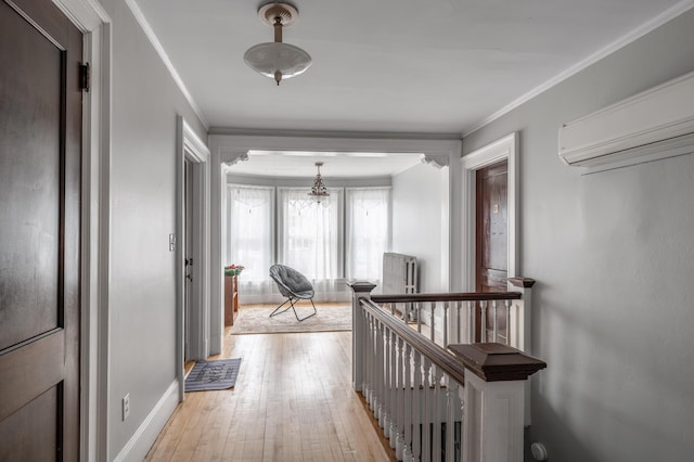 hall featuring baseboards, ornamental molding, a wall mounted air conditioner, an upstairs landing, and light wood finished floors