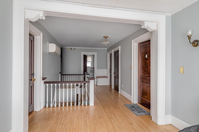 hallway with light wood-type flooring, a wall mounted air conditioner, ornamental molding, and an upstairs landing