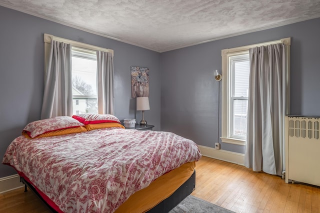 bedroom featuring ornamental molding, baseboards, radiator, and hardwood / wood-style floors