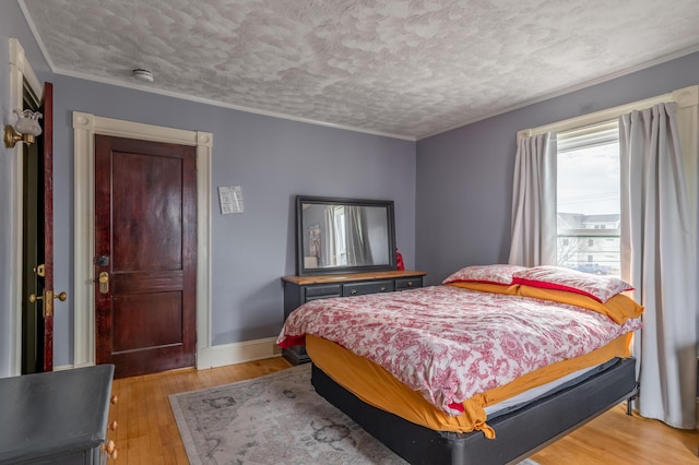 bedroom featuring crown molding, light wood finished floors, and a textured ceiling