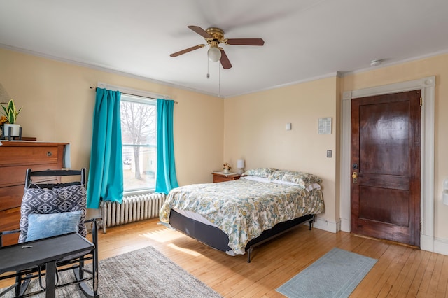 bedroom with radiator, a ceiling fan, ornamental molding, hardwood / wood-style floors, and baseboards