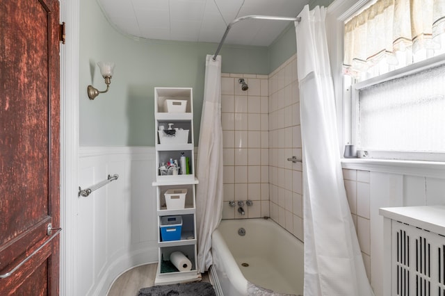 bathroom with shower / bath combination with curtain, a decorative wall, and a wainscoted wall