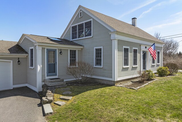view of front facade featuring roof with shingles, an attached garage, a chimney, and a front yard