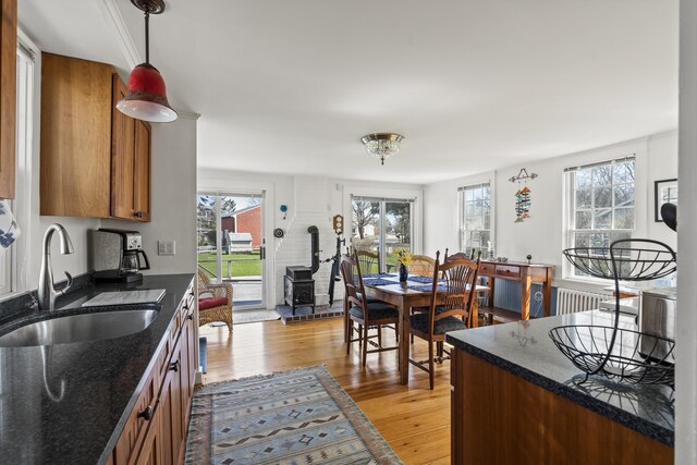 kitchen featuring brown cabinetry, a wood stove, light wood-type flooring, a sink, and decorative light fixtures