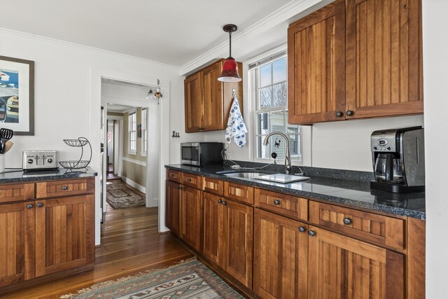kitchen with crown molding, a sink, dark stone counters, stainless steel microwave, and dark wood-type flooring