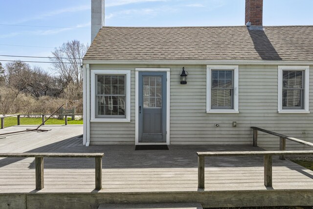 exterior space with a chimney, a shingled roof, and a wooden deck