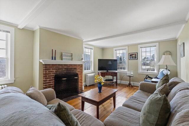 living area featuring a brick fireplace, hardwood / wood-style flooring, beam ceiling, baseboards, and radiator heating unit