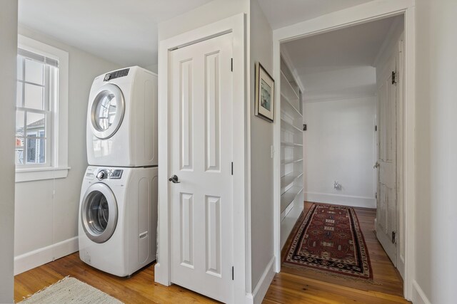 laundry area with baseboards, stacked washer / drying machine, light wood-style flooring, and laundry area