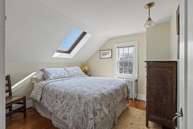 bedroom featuring baseboards, radiator heating unit, lofted ceiling with skylight, and wood finished floors