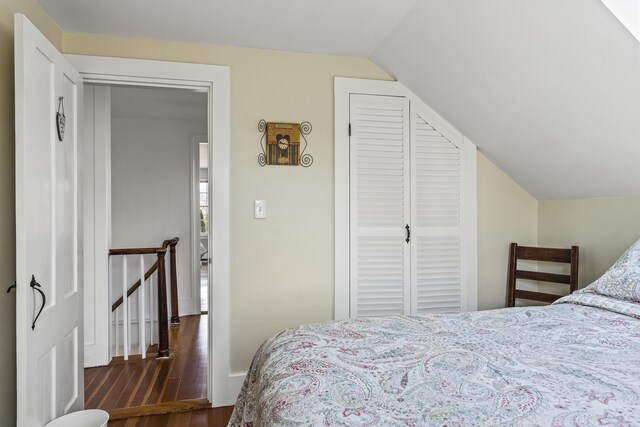 bedroom with baseboards, wood finished floors, lofted ceiling, and a closet