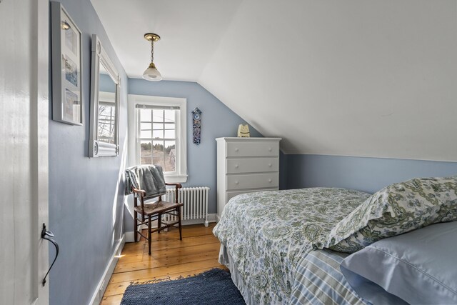 bedroom with baseboards, vaulted ceiling, radiator, and light wood-style floors