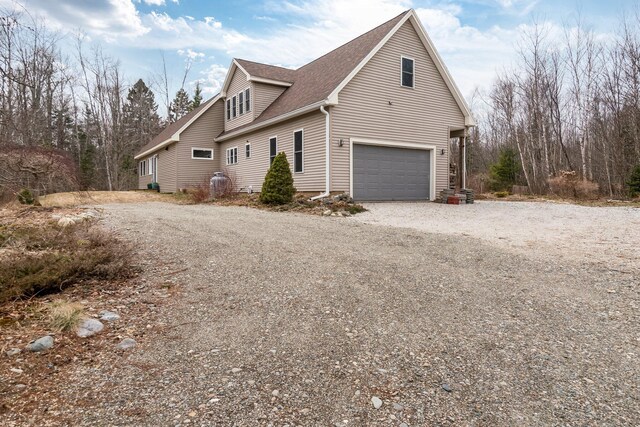 view of home's exterior featuring an attached garage, gravel driveway, and a shingled roof