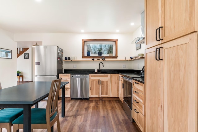 kitchen featuring light brown cabinets, dark countertops, a sink, appliances with stainless steel finishes, and dark wood-style floors