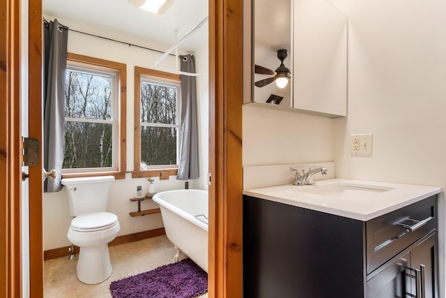 bathroom with a ceiling fan, vanity, a freestanding tub, baseboards, and toilet