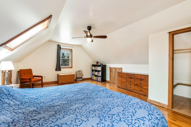 bedroom with ceiling fan, baseboards, vaulted ceiling with skylight, and wood finished floors