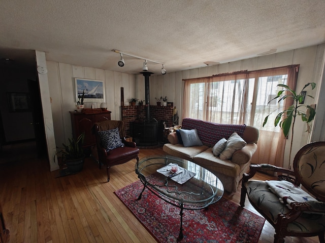 living area with a wood stove, light wood-style floors, rail lighting, and a textured ceiling