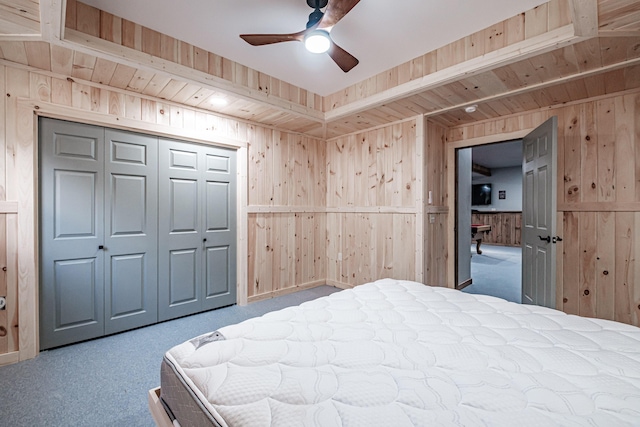 carpeted bedroom with wood walls, a closet, and a ceiling fan