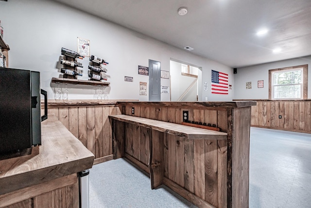 bar with light carpet, a dry bar, wooden walls, and wainscoting