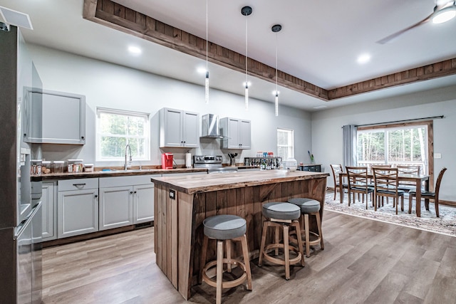 kitchen featuring wall chimney exhaust hood, butcher block counters, a center island, a sink, and light wood finished floors