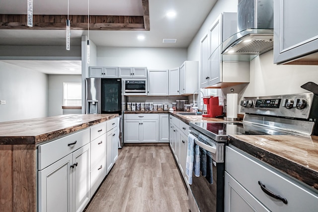 kitchen with wooden counters, built in microwave, wall chimney exhaust hood, electric stove, and a sink