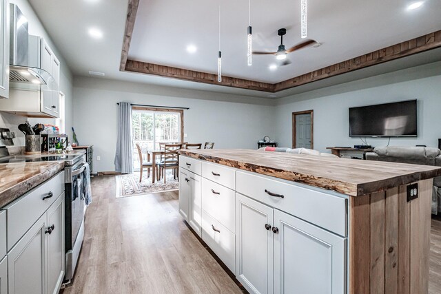 kitchen featuring a raised ceiling, light wood-style flooring, stainless steel range with electric stovetop, a center island, and butcher block countertops