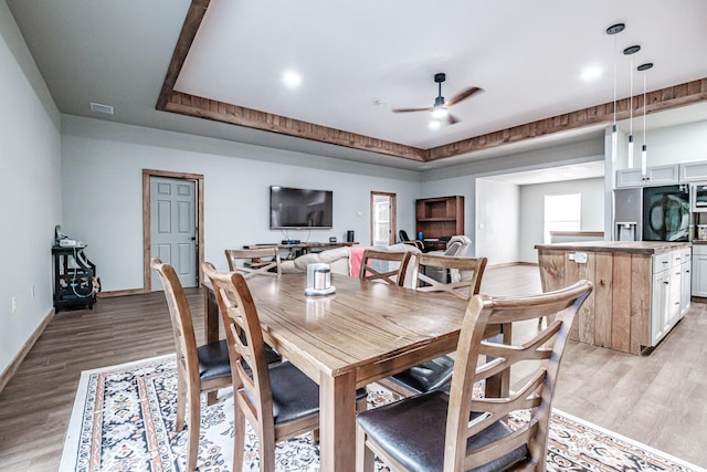 dining space with light wood-type flooring, baseboards, a raised ceiling, visible vents, and ceiling fan