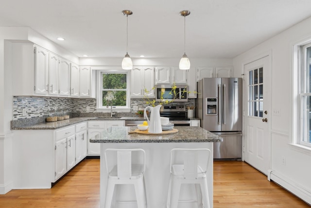 kitchen featuring stainless steel appliances, a baseboard heating unit, white cabinets, a sink, and backsplash