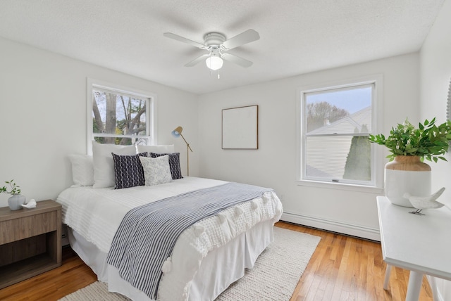 bedroom with a baseboard heating unit, light wood finished floors, and ceiling fan