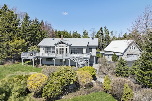 back of house featuring stairs, a detached garage, a deck, a chimney, and a lawn