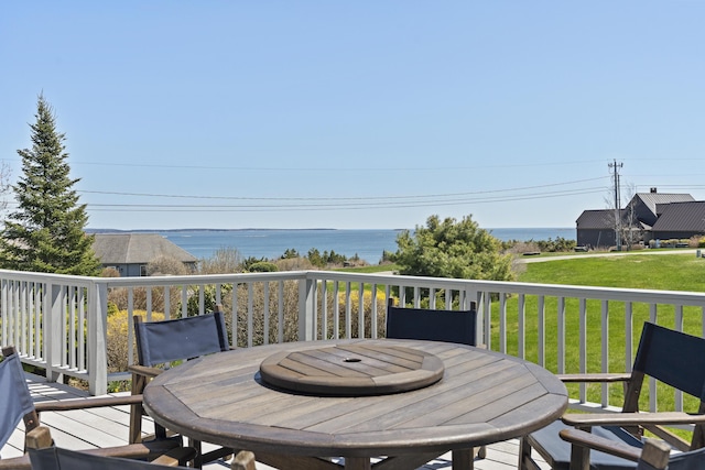 deck featuring outdoor dining area, a water view, and a lawn