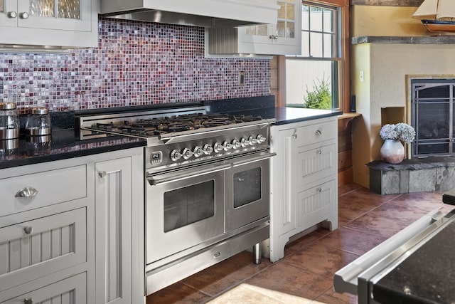 kitchen featuring wall chimney range hood, white cabinets, backsplash, and double oven range
