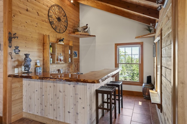 bar featuring wood walls, beamed ceiling, baseboards, high vaulted ceiling, and indoor bar