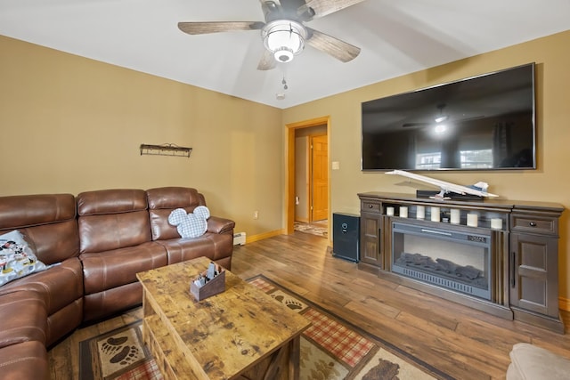 living area featuring ceiling fan, a baseboard heating unit, wood finished floors, and baseboards
