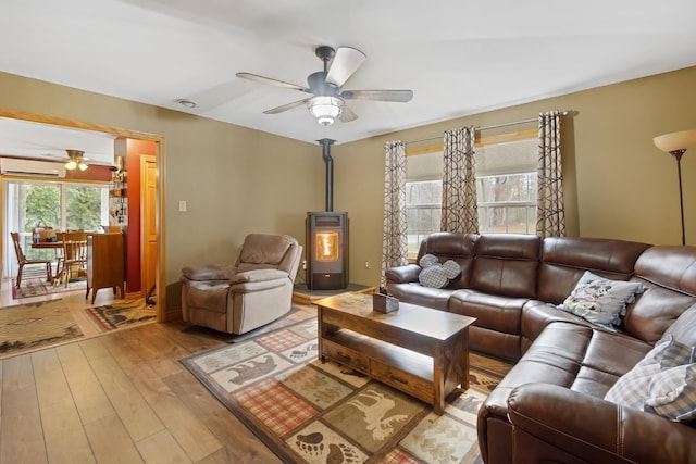living room featuring wood-type flooring, a wood stove, a ceiling fan, and a wall mounted AC