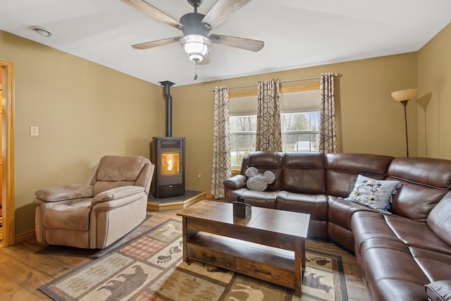 living room featuring a wood stove, a ceiling fan, and wood finished floors