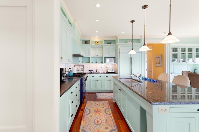 kitchen featuring a sink, dark wood finished floors, a center island with sink, high end stove, and backsplash