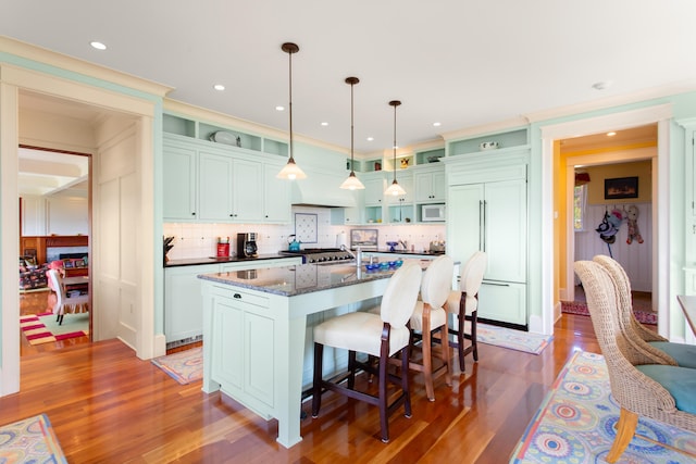 kitchen with a kitchen bar, wood finished floors, paneled built in refrigerator, and white microwave
