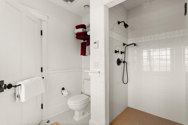 bathroom with a tile shower, toilet, a wainscoted wall, and tile patterned floors